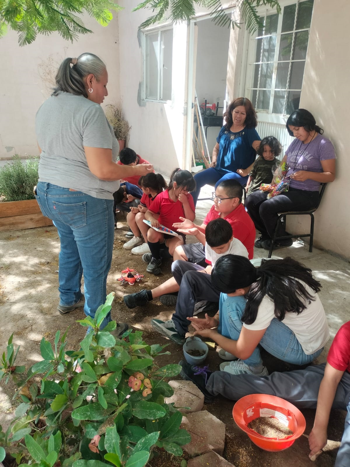 Selene explicando el huerto a un grupo de niños alrededor de una cama de cultivo
