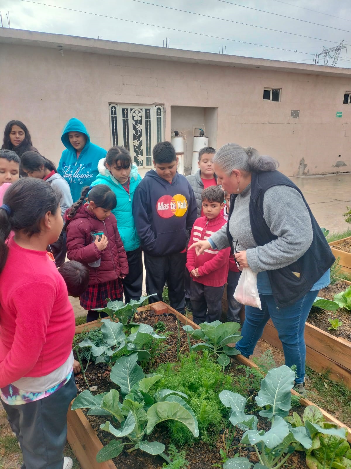 Niños y Selene sembrando juntos en una cama de cultivo durante un taller escolar